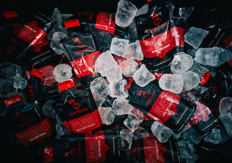 A pile of black and red Pure Tart Cherry flavor disposable vape packets mixed with clear ice cubes on a dark background.