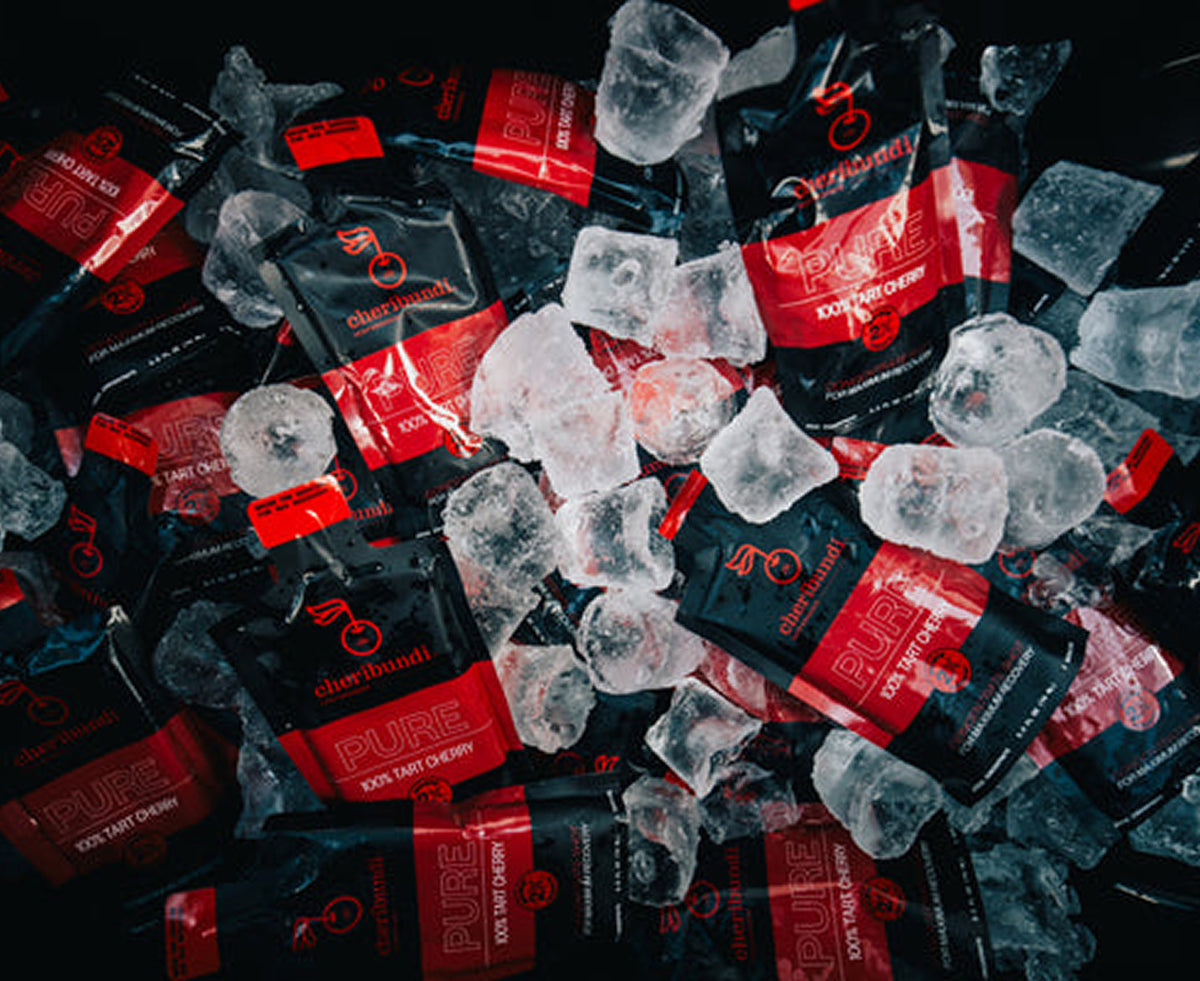 A pile of black and red Pure Tart Cherry flavor disposable vape packets mixed with clear ice cubes on a dark background.